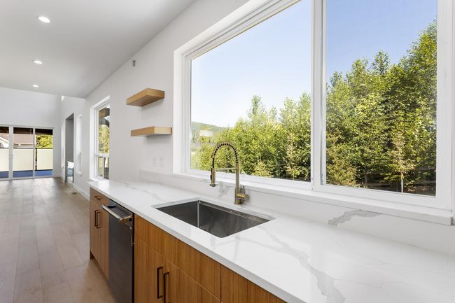 Kitchen with modern cabinets, a sink, open shelves, light stone countertops, and dishwasher | Image 10