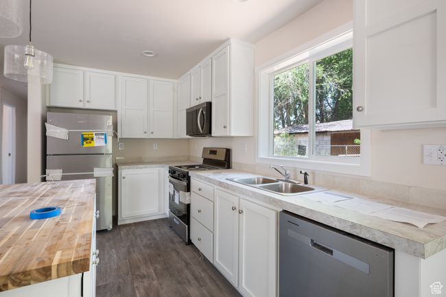 Kitchen with butcher block counters, stainless steel appliances, a sink, dark wood-style floors, and white cabinetry | Image 5