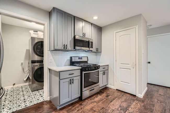 Kitchen with stainless steel appliances, gray cabinetry, estacked washer and dryer, light countertops, and decorative backsplash | Image 9