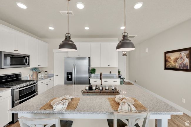 Kitchen featuring stainless steel appliances, a center island, a breakfast bar, white cabinetry, and light stone counters | Image 11
