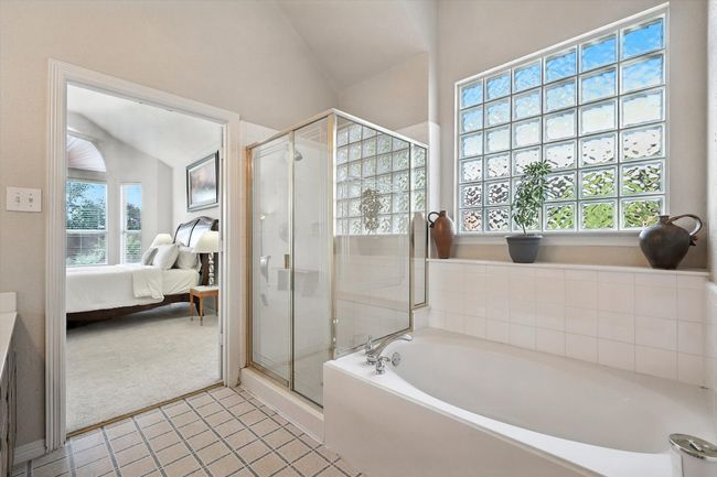 Ensuite bathroom featuring a bath, a stall shower, lofted ceiling, plenty of natural light, and tile patterned flooring | Image 23
