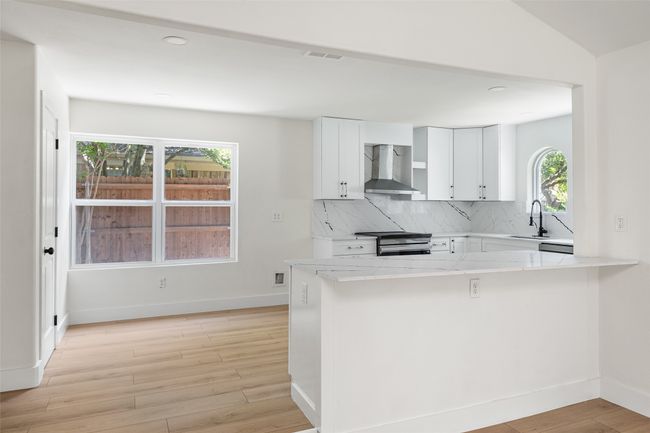 Kitchen featuring white cabinetry, light stone counters, decorative backsplash, wall chimney range hood, and light wood-style flooring | Image 9