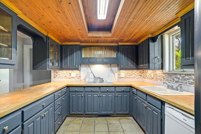 Kitchen featuring butcher block counters, wooden ceiling, updated backsplash, and glass insert cabinets | Image 8