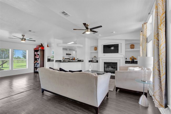Living room featuring ceiling fan, vaulted ceiling, built in shelves, dark wood-type flooring, and a tiled fireplace | Image 6