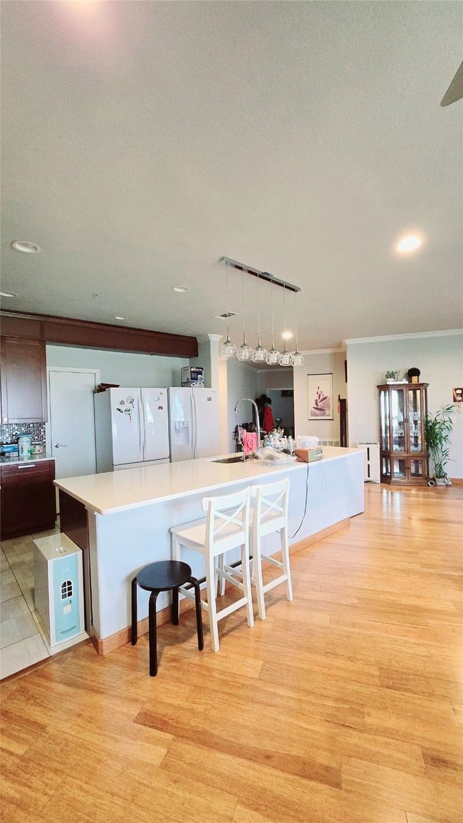 Kitchen with light wood-type flooring, recessed lighting, white refrigerator with ice dispenser, hanging light fixtures, and light countertops | Image 4