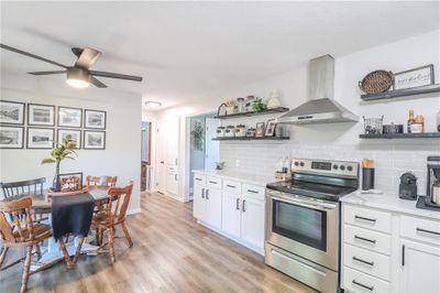 Kitchen with light wood-type flooring, tasteful backsplash, ventilation hood, white cabinetry, and stainless steel electric range oven | Image 3