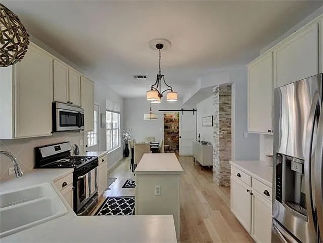 Kitchen featuring appliances with stainless steel finishes, a center island, light wood-type flooring, a barn door, and pendant lighting | Image 10