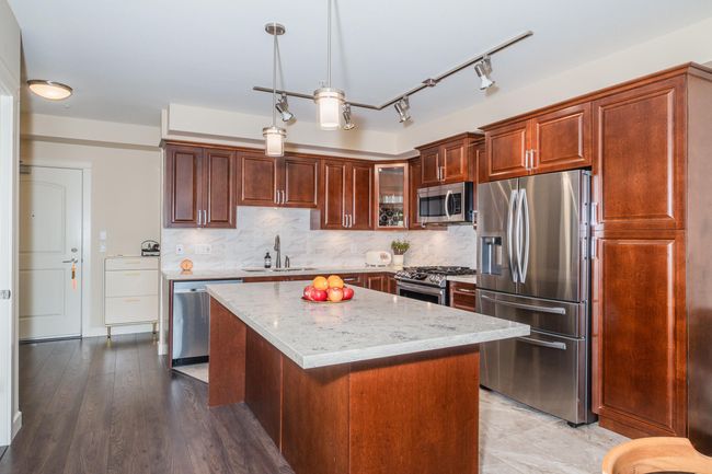 Kitchen with stainless steel appliances, a sink, light stone countertops, pendant lighting, and a kitchen island | Image 15