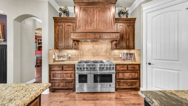 Kitchen with range with two ovens, custom exhaust hood, crown molding, light stone countertops, and tasteful backsplash | Image 21