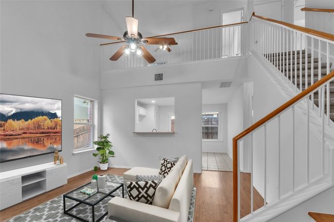Living area with stairs, ceiling fan, wood finished floors, and a high ceiling | Image 5