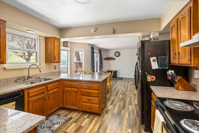 Kitchen with brown cabinets, a sink, light wood-type flooring, a peninsula, and dishwasher | Image 6