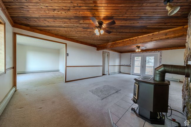 Unfurnished living room featuring a wood stove, wooden ceiling, carpet flooring, and ceiling fan | Image 6