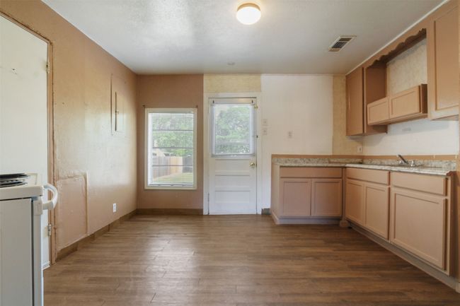 Kitchen with dark wood-style flooring, baseboards, white stove, visible vents, and a sink | Image 4