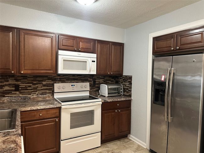 Kitchen with tasteful backsplash, white appliances, a textured ceiling, a toaster, and dark countertops | Image 4