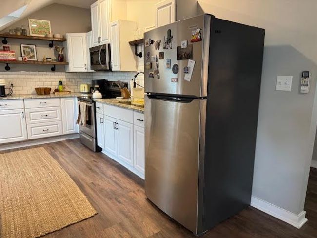 Kitchen featuring appliances with stainless steel finishes, dark wood-style floors, decorative backsplash, white cabinets, and lofted ceiling | Image 13