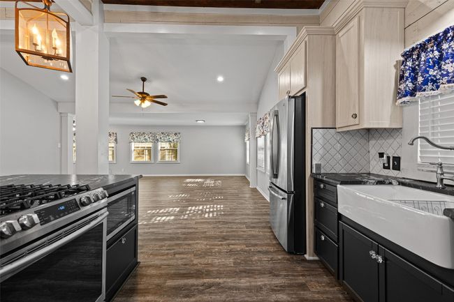 Kitchen featuring backsplash, dark countertops, a sink, appliances with stainless steel finishes, and dark wood-style flooring | Image 6