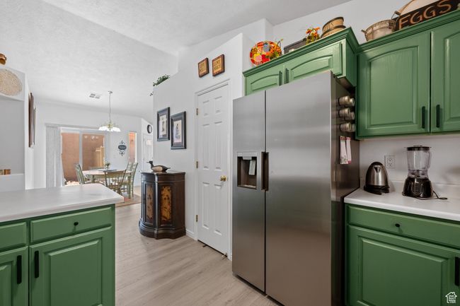 Kitchen featuring a textured ceiling, a chandelier, light countertops, light wood-type flooring, and stainless steel refrigerator with ice dispenser | Image 10