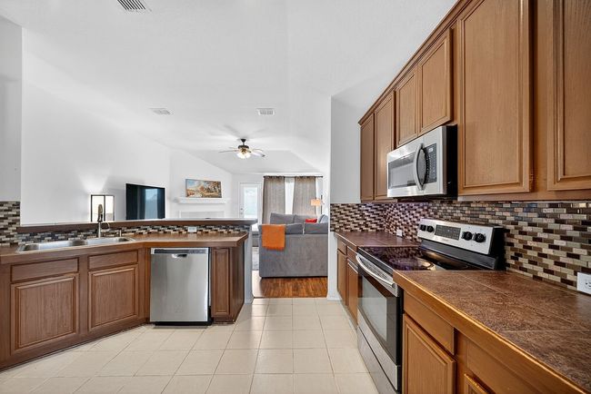 Kitchen with stainless steel appliances, dark countertops, open floor plan, ceiling fan, and backsplash | Image 16