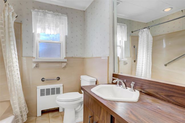 Bathroom with wallpapered walls, toilet, radiator heating unit, and tile patterned flooring | Image 12