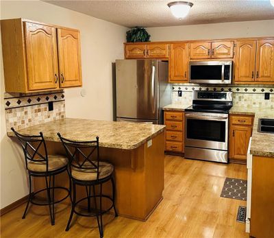 Kitchen featuring kitchen peninsula, tasteful backsplash, appliances with stainless steel finishes, a kitchen breakfast bar, and light wood-type flooring | Image 3