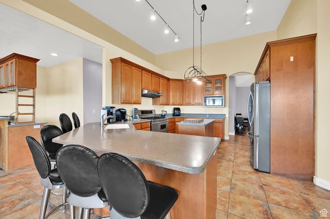 Kitchen with a peninsula, a kitchen bar, a sink, stainless steel appliances, and under cabinet range hood | Image 20