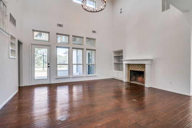 Unfurnished living room with a high ceiling, hardwood / wood-style flooring, a chandelier, built in features, and a fireplace | Image 7