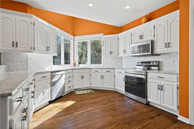 Kitchen featuring stainless steel appliances, dark hardwood floors, white cabinetry, and vaulted ceiling | Image 3