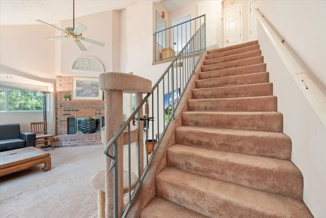 Stairs with carpet, high vaulted ceiling, a brick fireplace, ceiling fan, and a textured ceiling | Image 20