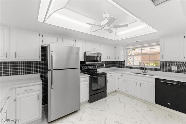 Kitchen featuring white cabinetry, light tile patterned floors, ceiling fan, black appliances, and sink | Image 17