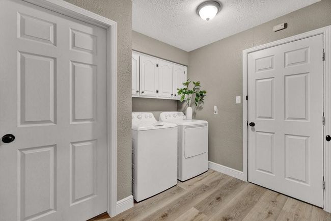 Laundry area featuring a textured wall, a textured ceiling, washing machine and clothes dryer, light wood finished floors, and cabinet space | Image 21