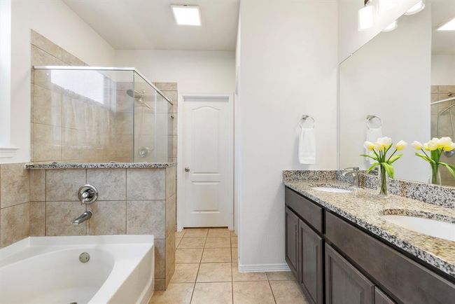 This stylish primary bathroom features dual sinks, rich stained cabinetry with granite countertops, a walk-in shower, and a relaxing soaker tub. | Image 23