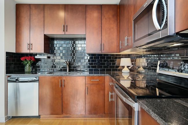 Kitchen with appliances with stainless steel finishes, a sink, dark stone countertops, and backsplash | Image 6