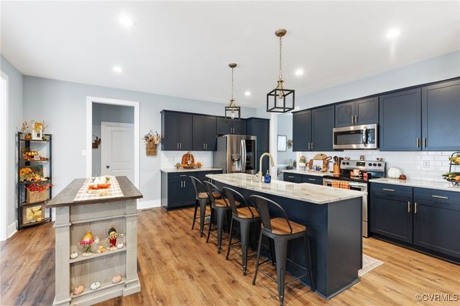 Kitchen with a kitchen breakfast bar, tasteful backsplash, light stone countertops, stainless steel appliances, and an island with sink | Image 5