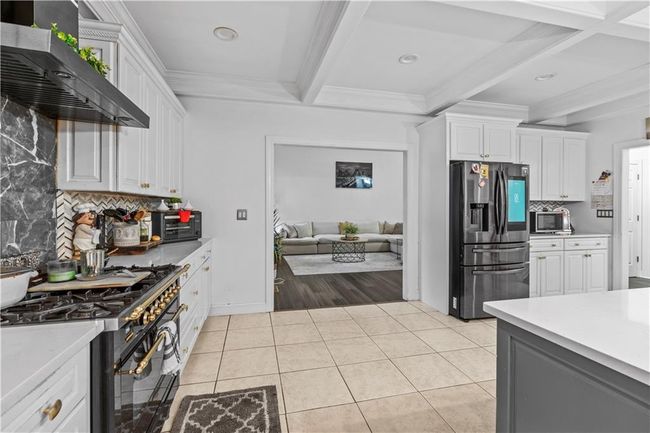 Kitchen featuring appliances with stainless steel finishes, beam ceiling, wall chimney exhaust hood, tasteful backsplash, and light countertops | Image 9
