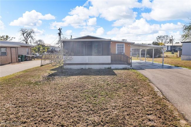 View of front of property featuring aphalt driveway, an attached carport, a sunroom, a front yard, and stucco siding | Image 4