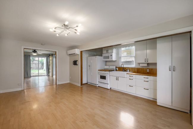 Kitchen with white appliances, a wall unit AC, ceiling fan, light wood-type flooring, and baseboards | Image 20
