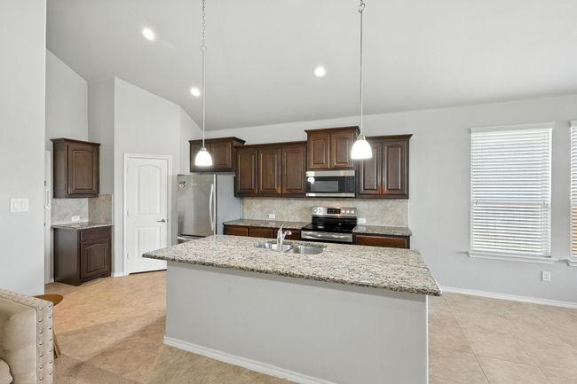 Kitchen with appliances with stainless steel finishes, dark brown cabinets, backsplash, light tile patterned floors, and recessed lighting | Image 5
