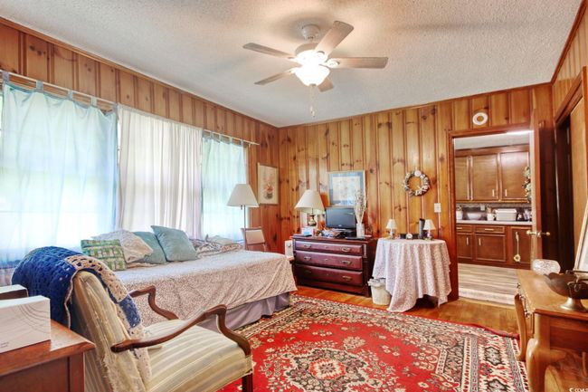 Bedroom featuring light wood-style flooring, wood walls, a textured ceiling, and a ceiling fan | Image 18