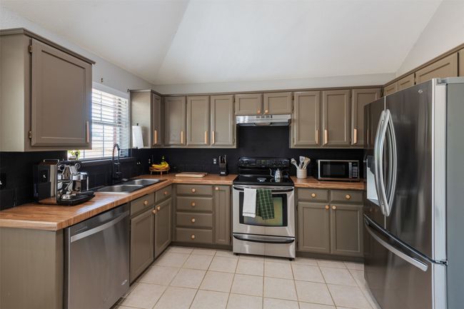 Kitchen with stainless steel appliances, vaulted ceiling, under cabinet range hood, light tile patterned floors, and gray cabinetry | Image 8