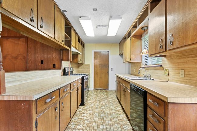 Kitchen with double oven range, black dishwasher, under cabinet range hood, open shelves, and a textured ceiling | Image 7
