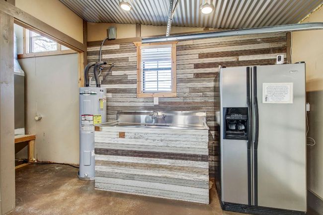 Kitchen featuring wood walls, stainless steel fridge, unfinished concrete flooring, electric water heater, and vaulted ceiling | Image 27