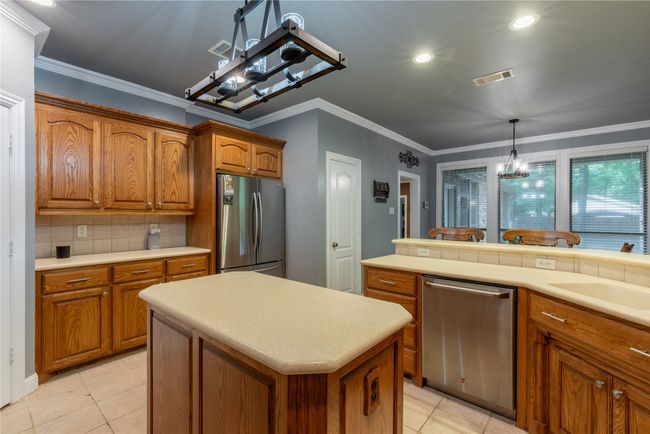 Kitchen featuring appliances with stainless steel finishes, brown cabinetry, a chandelier, light countertops, and ornamental molding | Image 14
