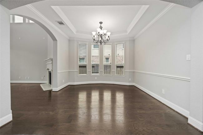 Spacious dining room with elegant hardwood floors, crown molding, and a stylish chandelier. The room features large windows for ample natural light and an adjacent view into a living area with a fireplace. | Image 9