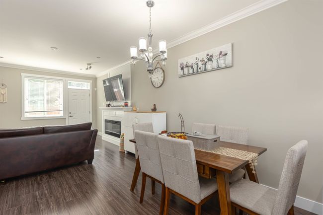 Dining space featuring crown molding, a chandelier, wood finished floors, a glass covered fireplace, and baseboards | Image 16
