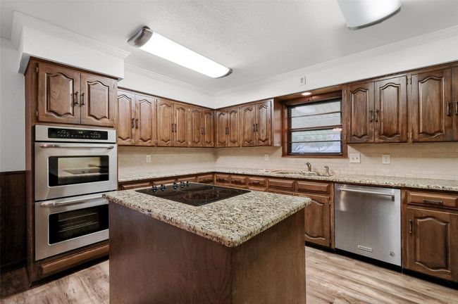 Kitchen featuring appliances with stainless steel finishes, a sink, light wood-style flooring, crown molding, and a center island | Image 10