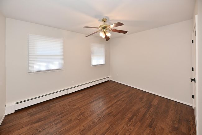 Empty room with a ceiling fan, dark wood-style floors, baseboard heating, and baseboards | Image 21