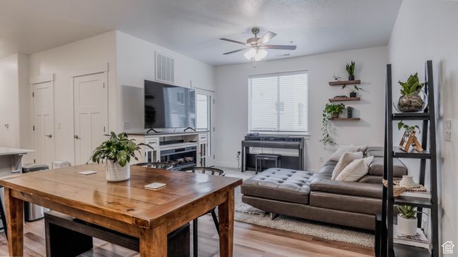 Living area with a ceiling fan, light wood finished floors, a fireplace, baseboards, and visible vents | Image 7