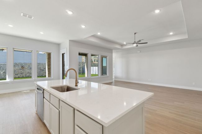 Kitchen featuring a tray ceiling, open floor plan, light wood-style floors, a ceiling fan, and an island with sink | Image 16