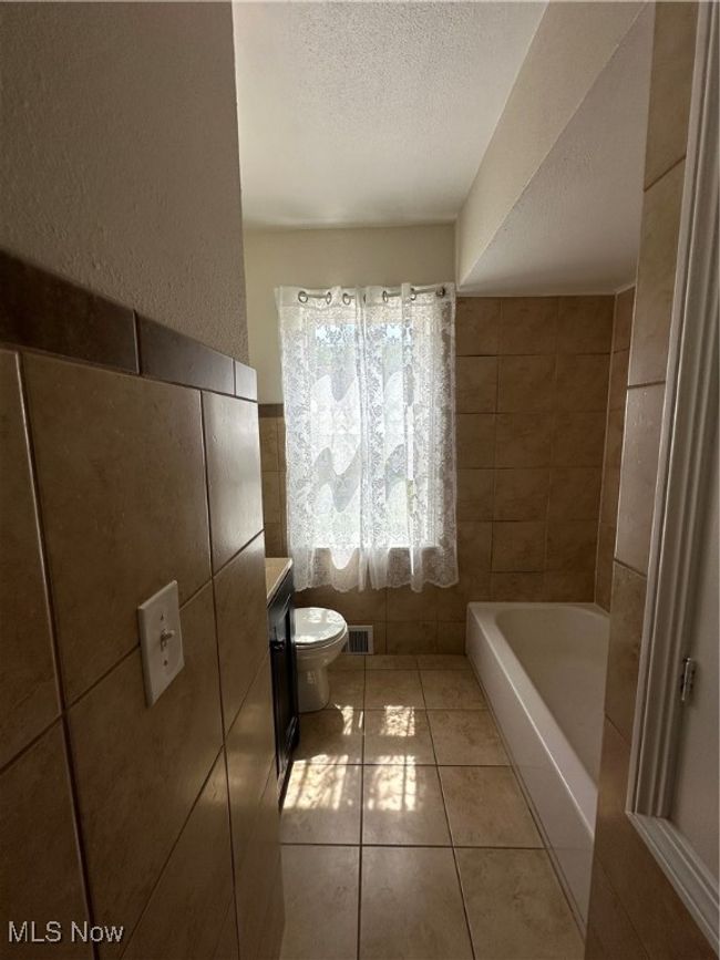 Bathroom featuring a textured ceiling, a tub to relax in, visible vents, tile walls, and tile patterned floors | Image 24