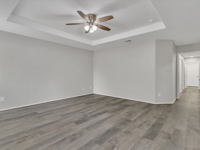 Empty room with a tray ceiling, ceiling fan, wood finished floors, and baseboards | Image 12